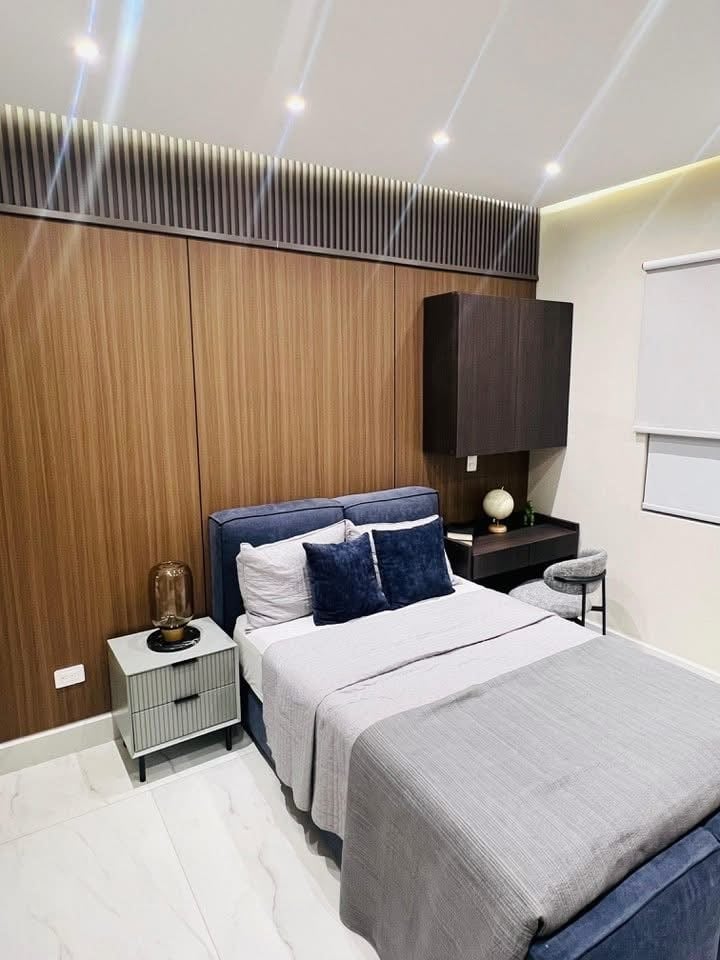 Modern bedroom with blue bedding, wood accent wall, floating black nightstand, and recessed ceiling lights