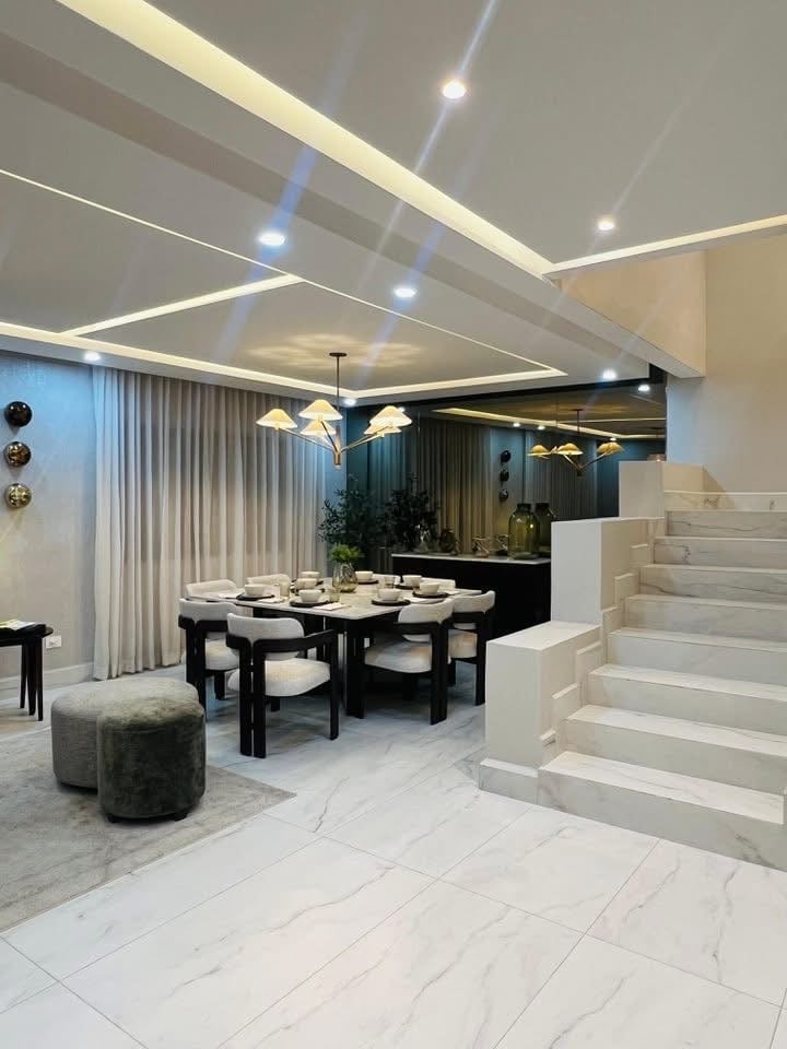 Modern open-concept dining area with black table, white chairs, recessed ceiling lights, white marble flooring, and white staircase