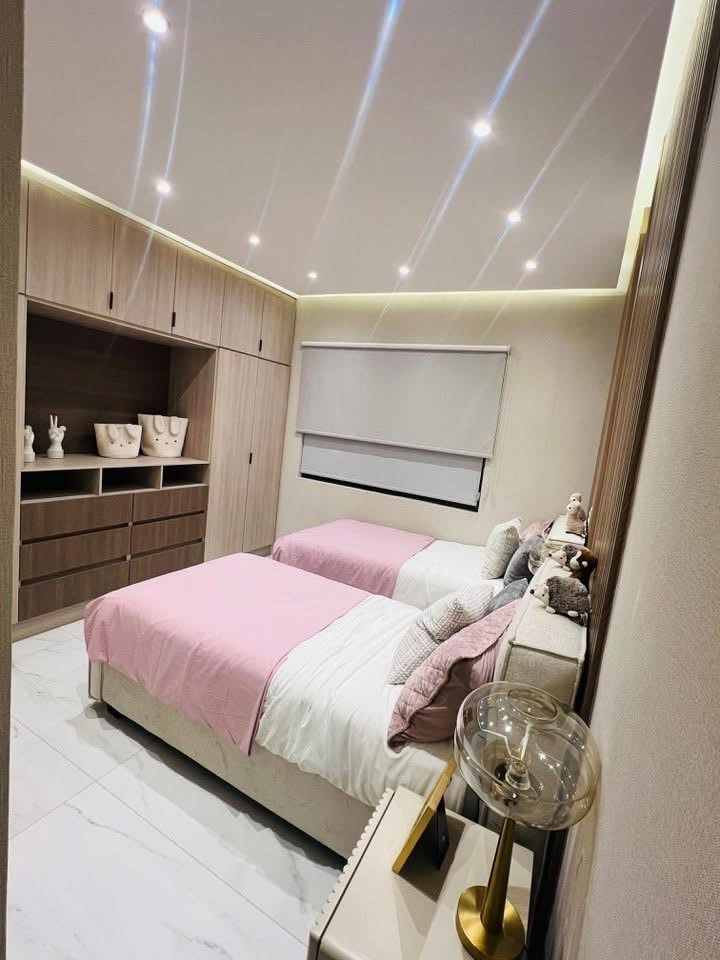 Modern bedroom with pink and white bedding, wooden storage cabinets, recessed ceiling lights, and minimalist decor